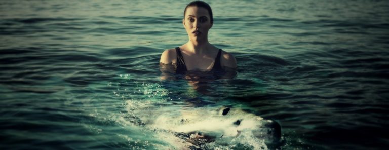Eine Frau im Wasser schaut ängstlich auf den Hai, der vor ihr auftaucht.