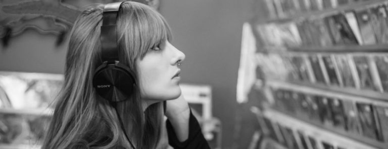 Eine junge Frau mit Kopfhörern sieht sich ein CD-Regal an.